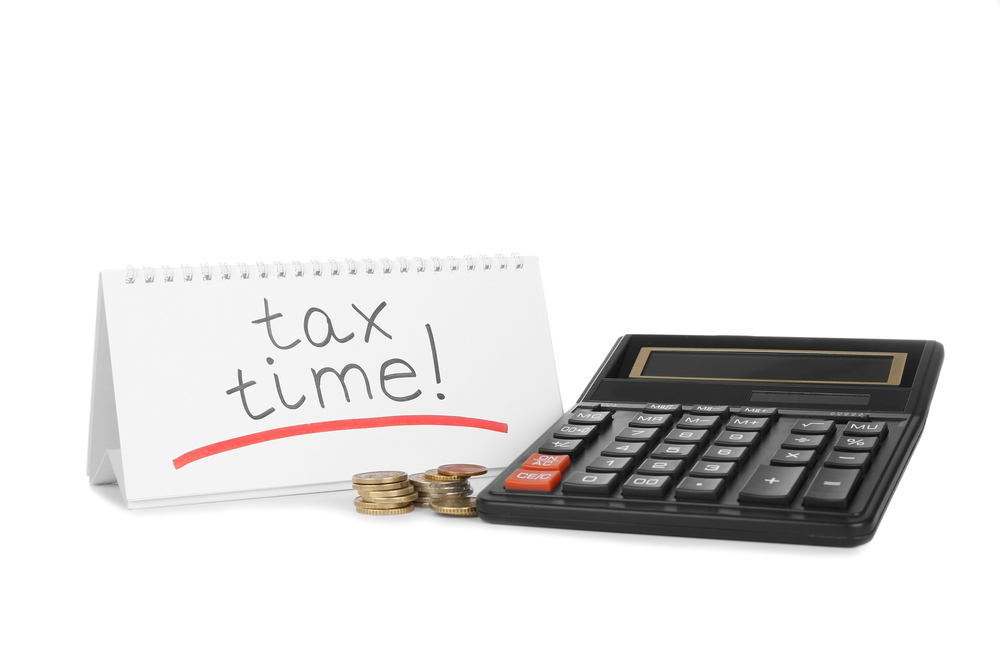 Tax time written on calendar beside calculator and coins